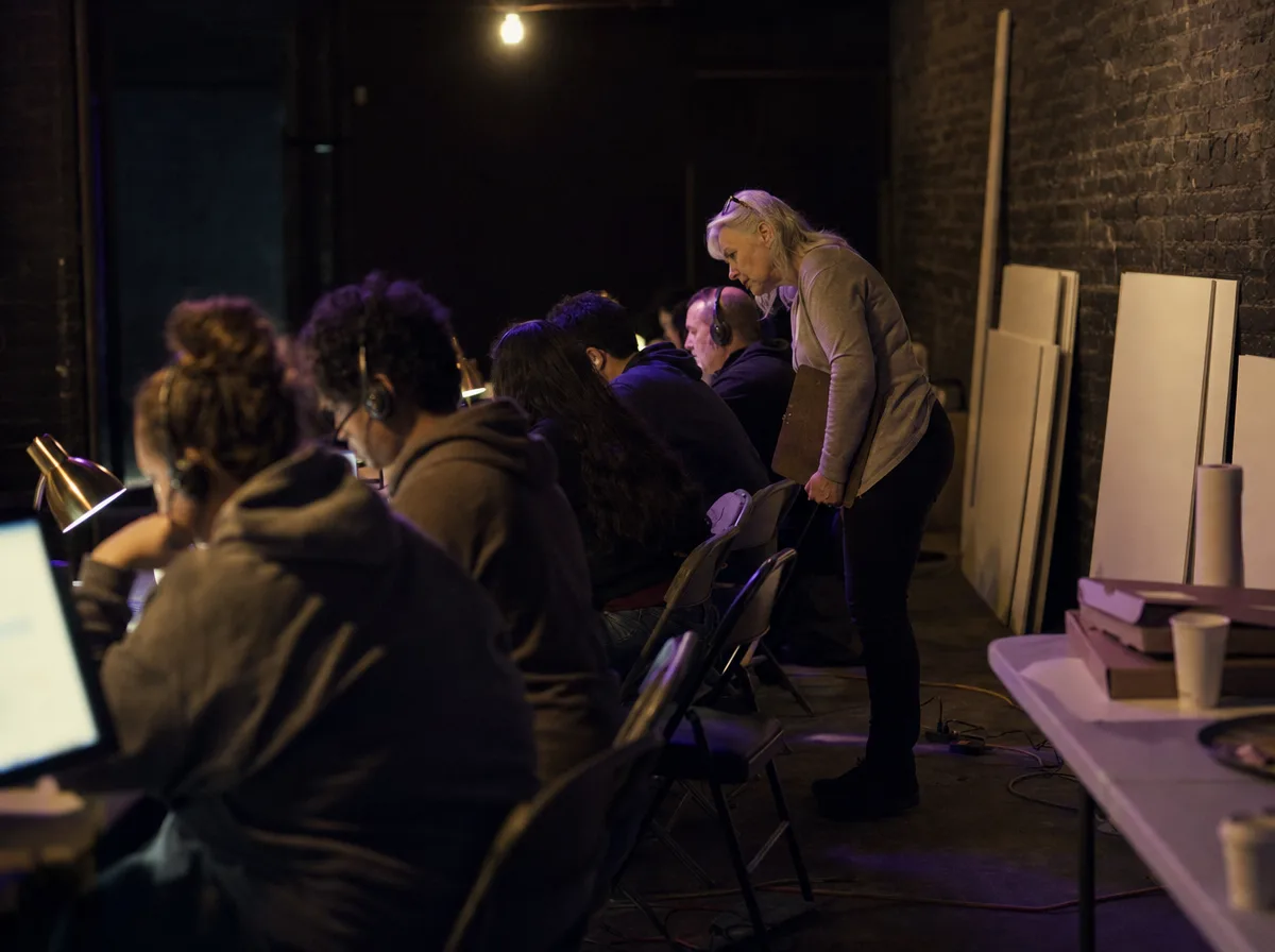 Volunteers in headsets at folding tables in a campaign office at night as an organizer leans in.