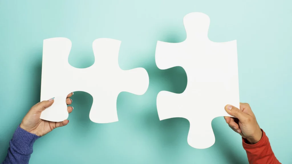Two hands, each holding a large white puzzle piece against a light blue background, with the pieces positioned close together as if about to connect-a visual metaphor often used by Dharmesh Shah for collaboration and problem-solving. VoiceDrop Ringless Voicemails