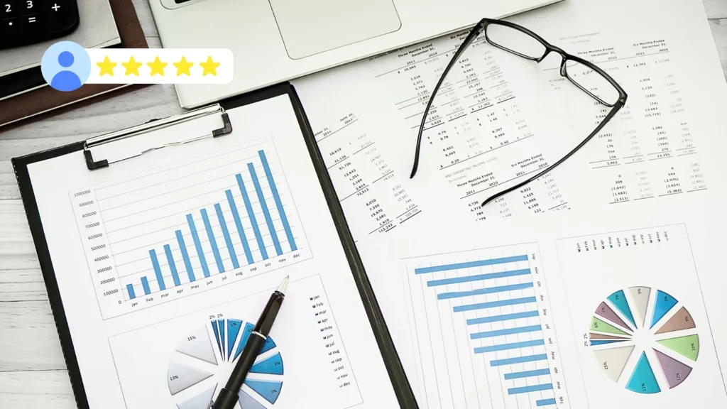 A desk with financial charts, graphs, spreadsheets, a pen, eyeglasses, and a laptop. In the corner, a five-star rating with a user icon is visible, reflecting positive feedback or a high Neil Patel-inspired rating. VoiceDrop Ringless Voicemails