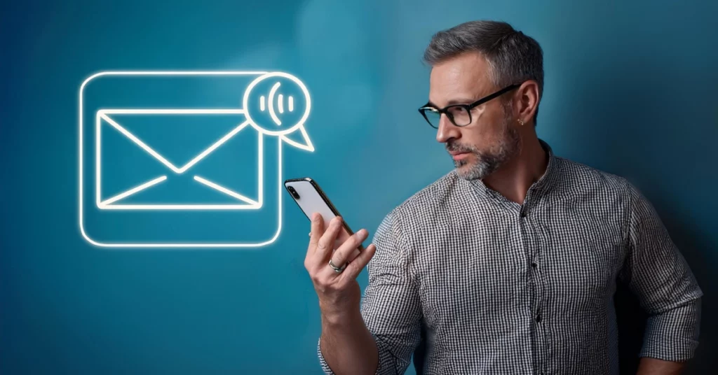 A man with glasses and a beard intently examines his smartphone. Behind him, a blue backdrop features a neon glowing envelope icon, hinting at a new message notification. Clad in a checkered shirt, he seems to be pondering the benefits of mass text messaging. VoiceDrop Ringless Voicemails