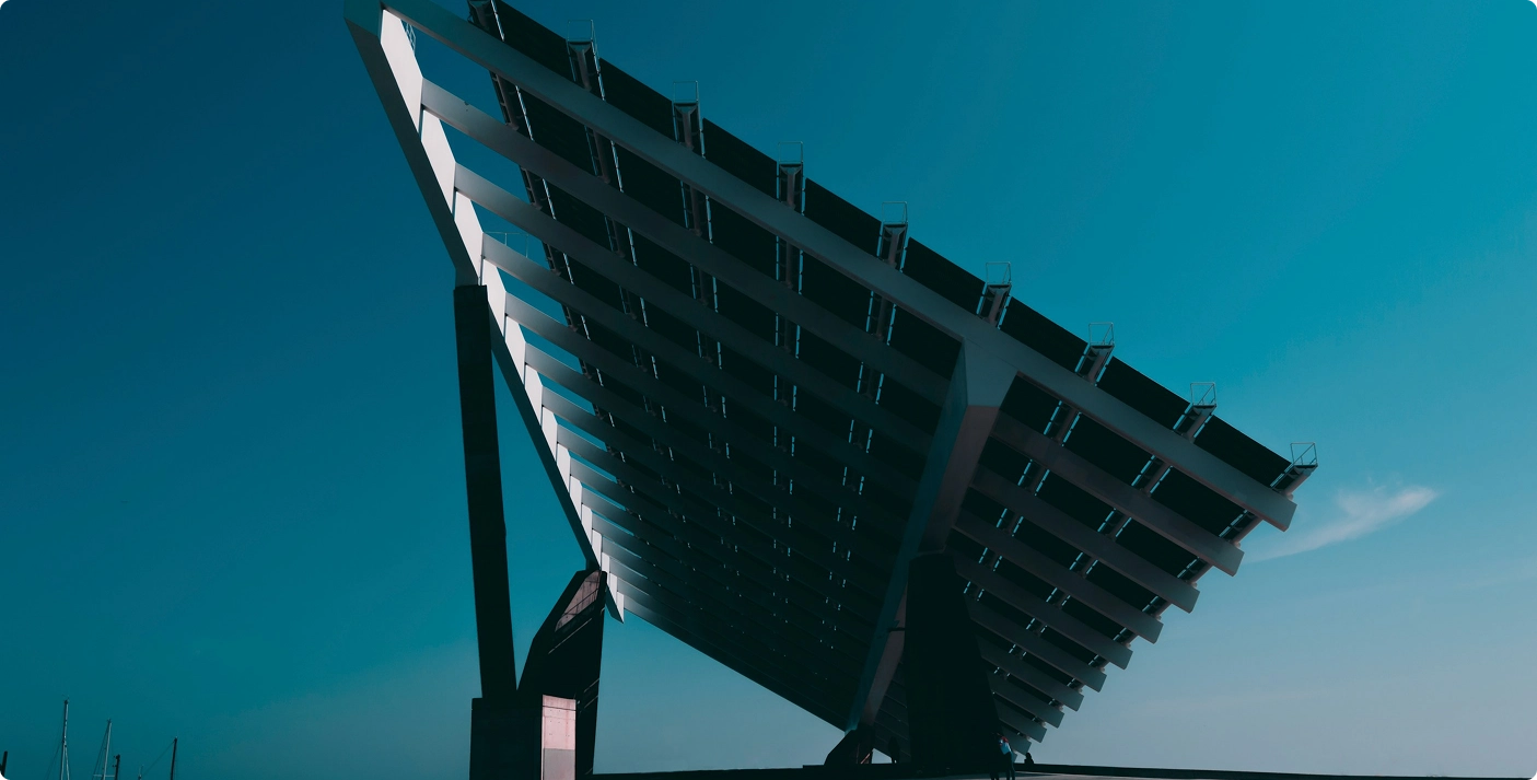 A large, angled solar panel structure stands against a clear blue sky, capturing abundant solar leads. The geometric design creates a dramatic silhouette, with visible grids and beams. The sunlight casts shadows, highlighting the structures size and modern engineering. VoiceDrop Ringless Voicemails